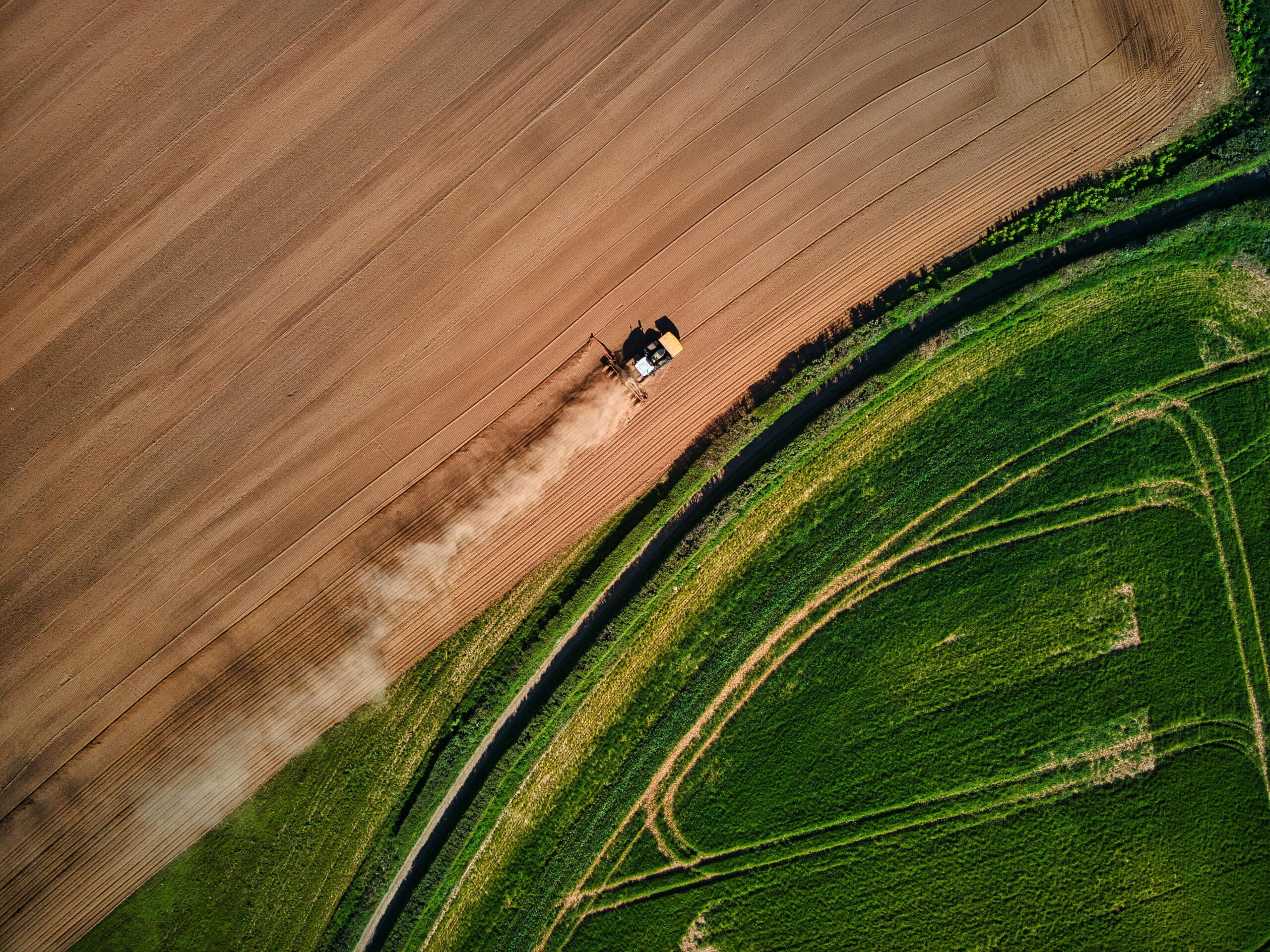 Drone shot of a tractor working a field with vibrant green and brown tones.