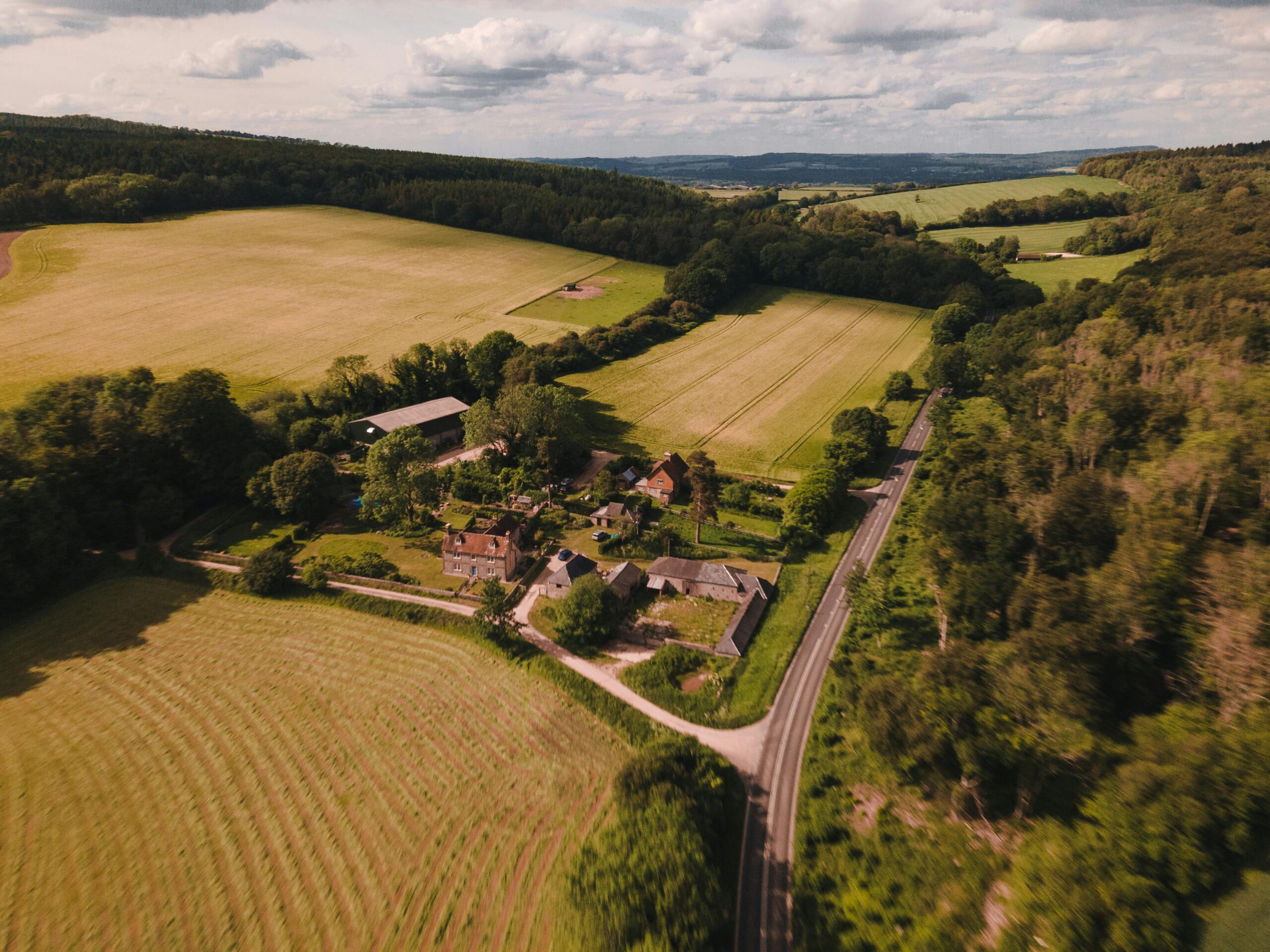 A scenic aerial view showcasing a farmhouse amid lush green fields in West Sussex, England.